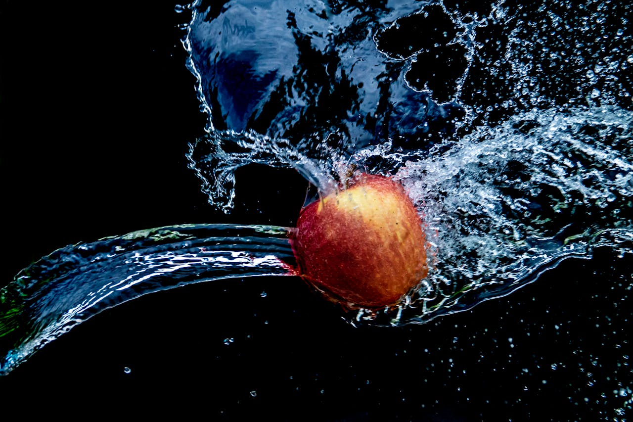 A red apple breaking through water splash with high contrast background.
